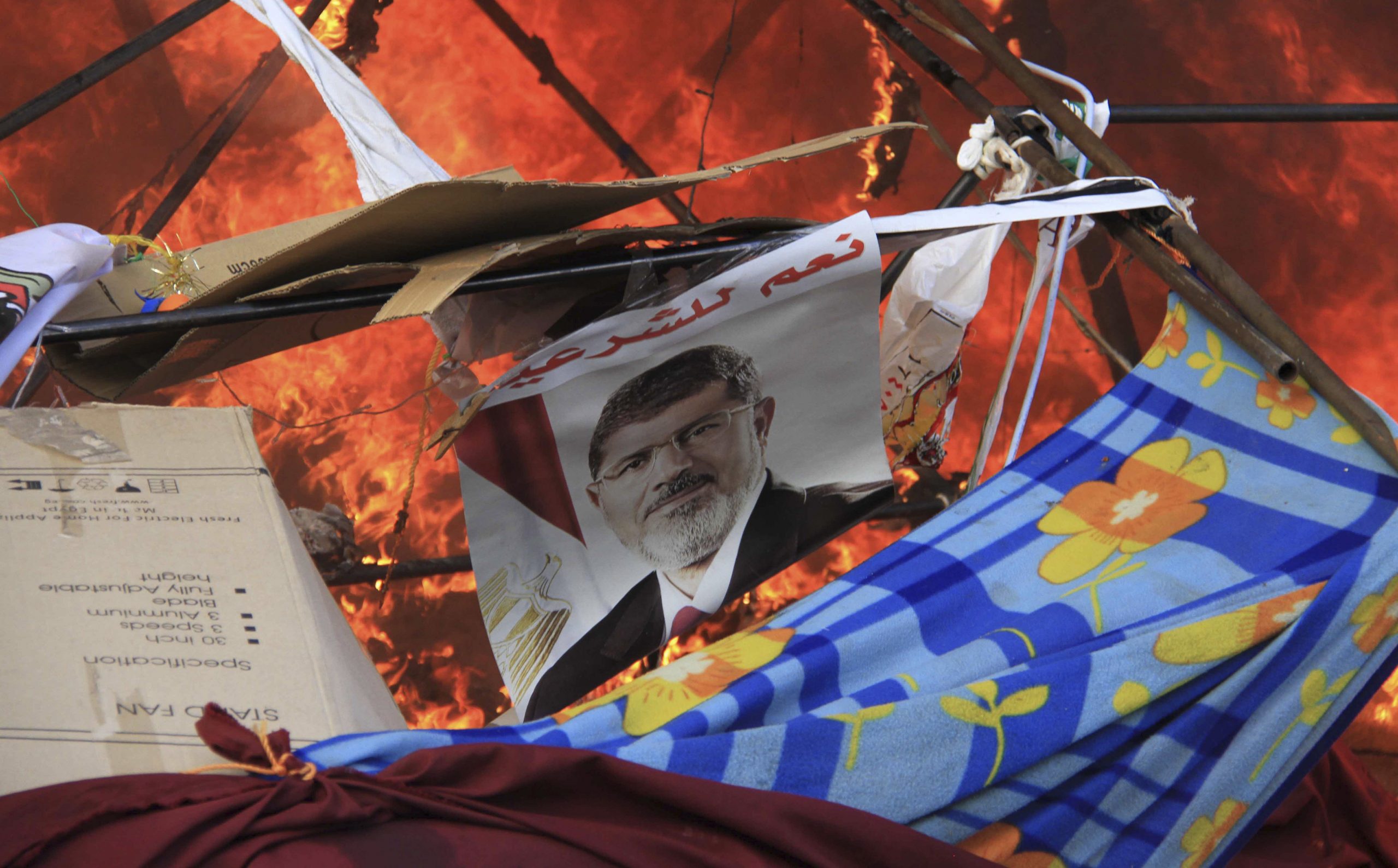 A poster of ُEgypt's former president Mohamed Morsi reads "Yes to legitimacy" as riot police clears the area of members of the Muslim Brotherhood and supporters at Rabaa Adawiya square, where they were camping, hundreds of them were killed on that single event, Cairo, 14 August 2013. Reuters, Stringer.
