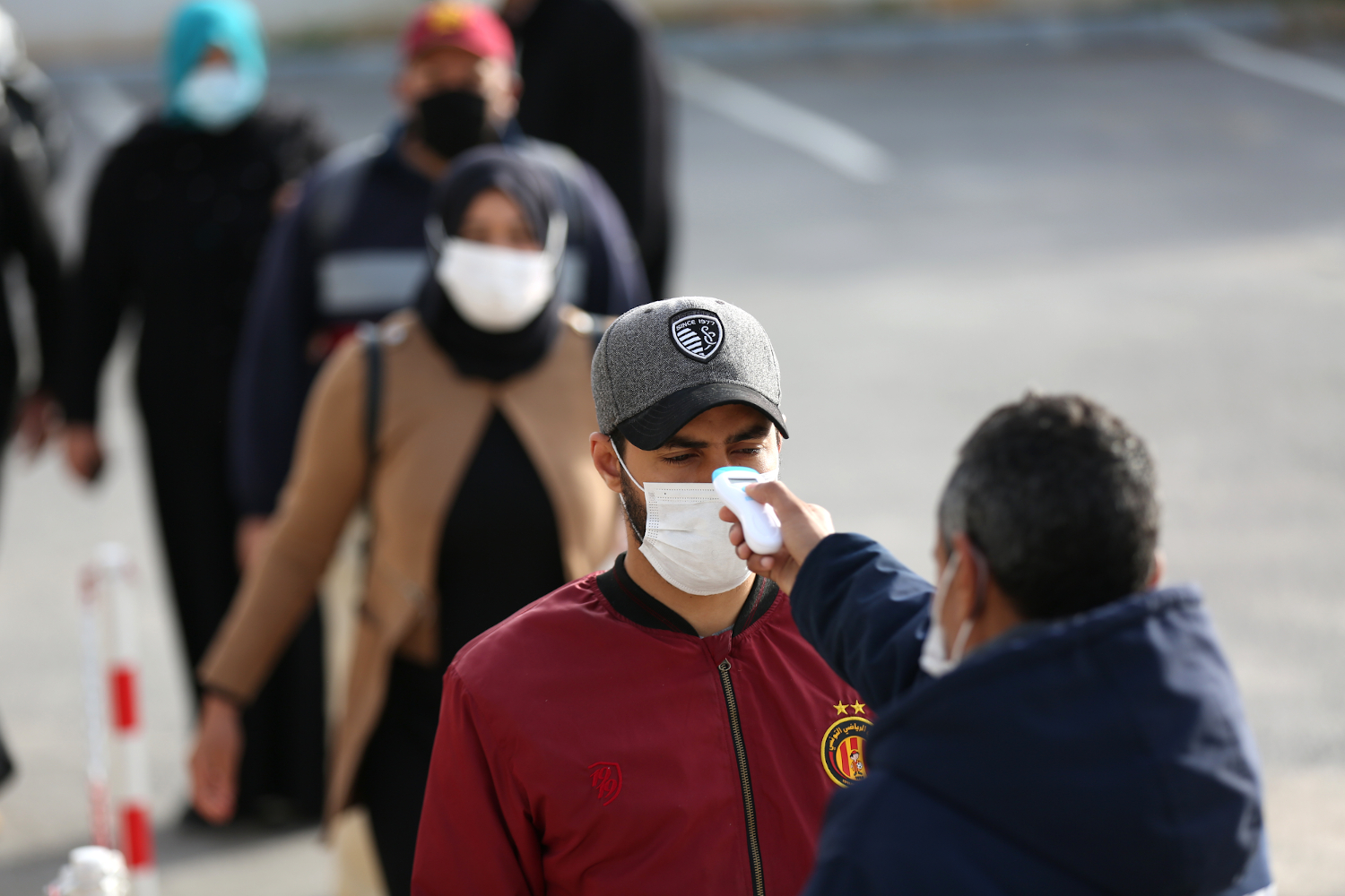 فرد حراسة أمنية يقوم بقياس درجات حرارة العمال في طابور بأحد مصانع مدينة منوبة بعد إعلان الحظر العام يوم 22 مارس 2020 لمجابهة جائحة كوفيد-19، تونس، 14 أبريل 2020. رويترز، محمد كريت.