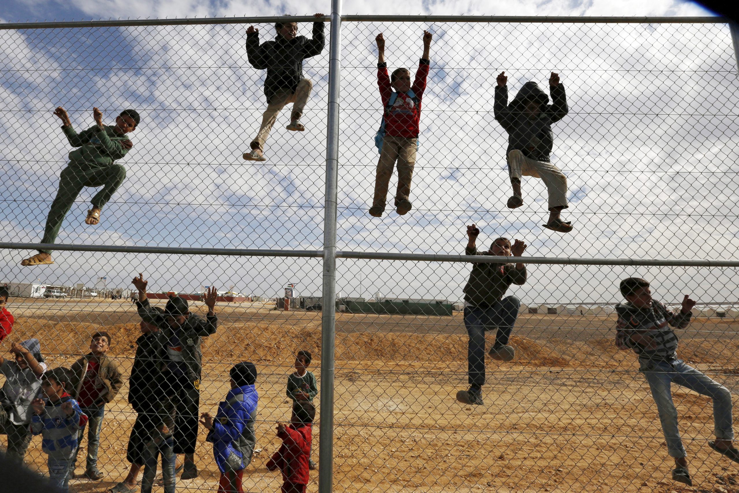 أطفال سوريون لاجئون يتسلقون على سياج من أجل مشاهدة ورشة تدريبية لكرة القدم بمخيم الأزرق للاجئين، الأردن، 17 نوفمبر 2015. رويترز، محمد حامد.